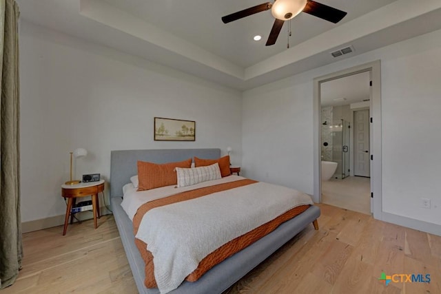 bedroom featuring a tray ceiling, baseboards, visible vents, and light wood-style flooring
