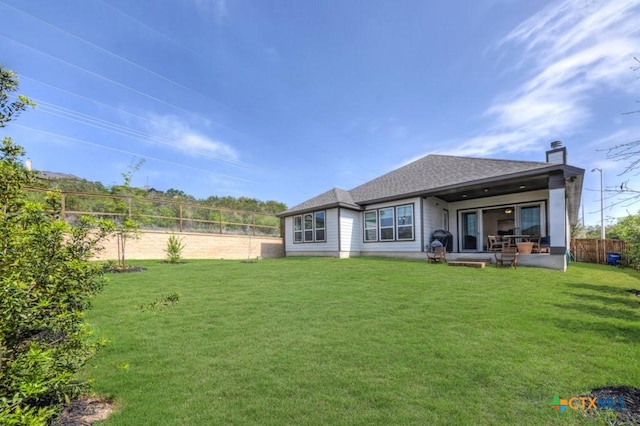 back of property with a fenced backyard, roof with shingles, a yard, and a chimney