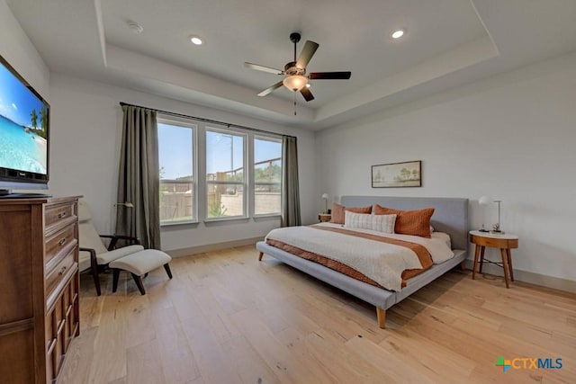 bedroom featuring baseboards, a tray ceiling, recessed lighting, and light wood-type flooring