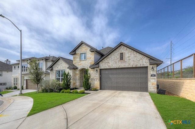 french country inspired facade with a front yard, stone siding, a garage, and concrete driveway