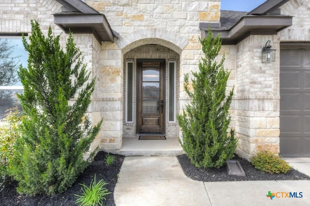 doorway to property featuring stone siding and a garage