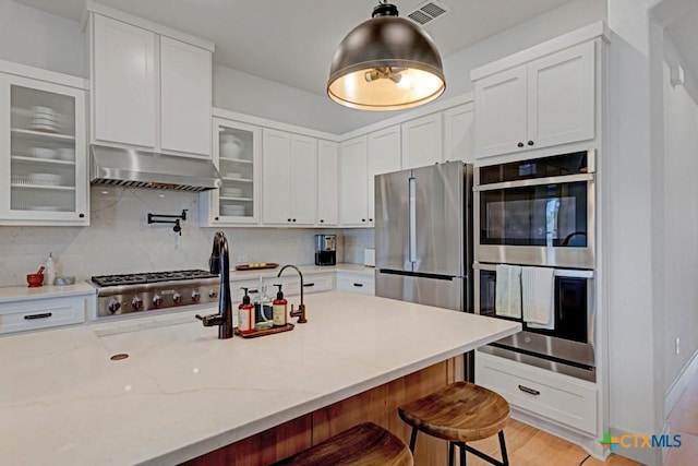 kitchen featuring tasteful backsplash, a breakfast bar area, stainless steel appliances, under cabinet range hood, and visible vents