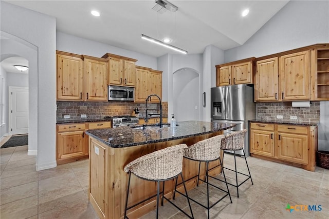 kitchen with arched walkways, lofted ceiling, a sink, stainless steel appliances, and backsplash