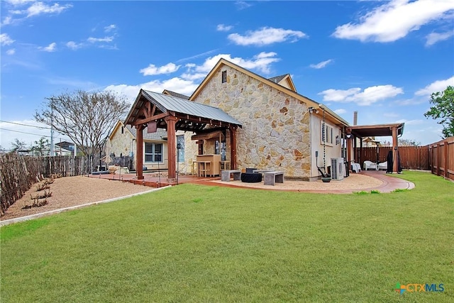 rear view of house featuring a patio, a fenced backyard, a gazebo, stone siding, and a lawn