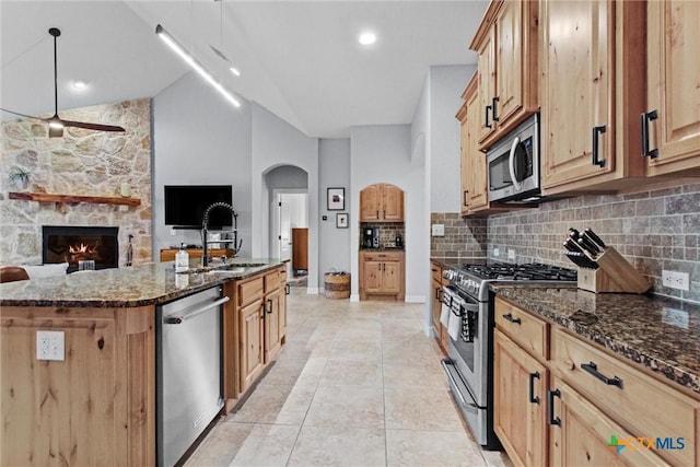 kitchen with arched walkways, stainless steel appliances, a sink, and dark stone counters