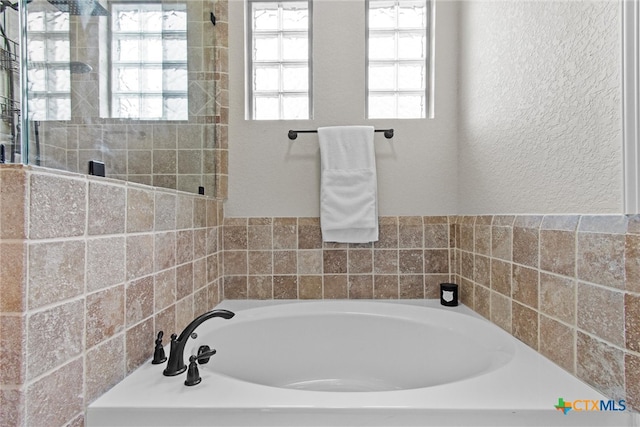 bathroom with a textured wall, a tile shower, and a bath