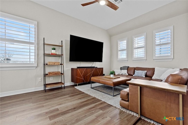 living area with visible vents, light wood-style flooring, vaulted ceiling, ceiling fan, and baseboards