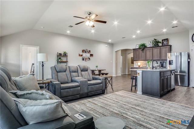 living room with hardwood / wood-style flooring, ceiling fan, sink, and vaulted ceiling