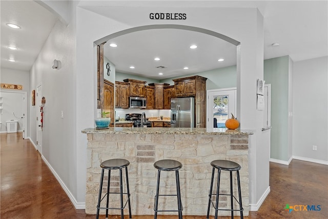 kitchen featuring kitchen peninsula, a kitchen bar, light stone counters, and appliances with stainless steel finishes