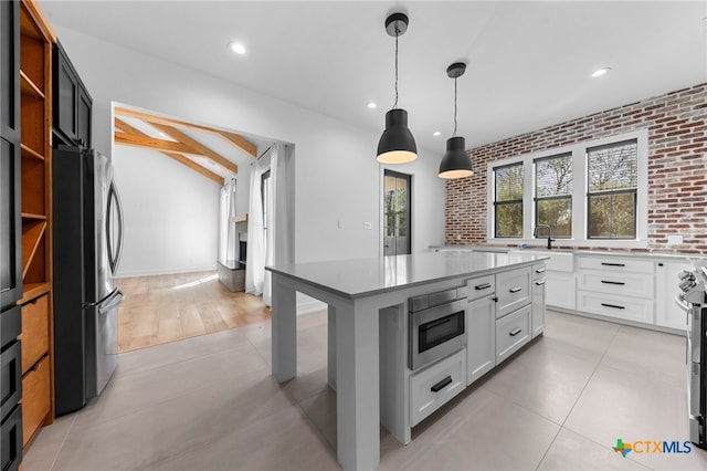 kitchen featuring white cabinets, brick wall, decorative light fixtures, a kitchen island, and appliances with stainless steel finishes