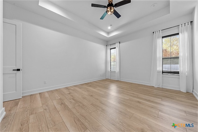 unfurnished room with light hardwood / wood-style floors, a raised ceiling, and ceiling fan