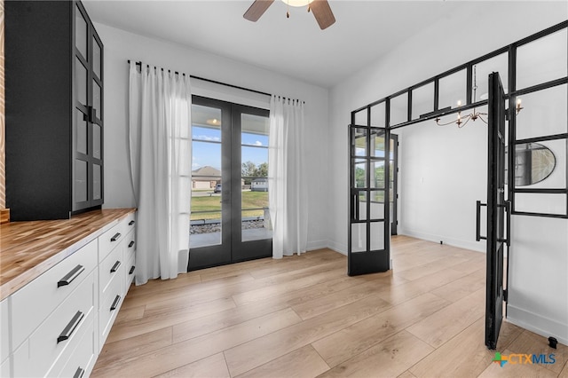 entryway with french doors, ceiling fan with notable chandelier, and light hardwood / wood-style flooring