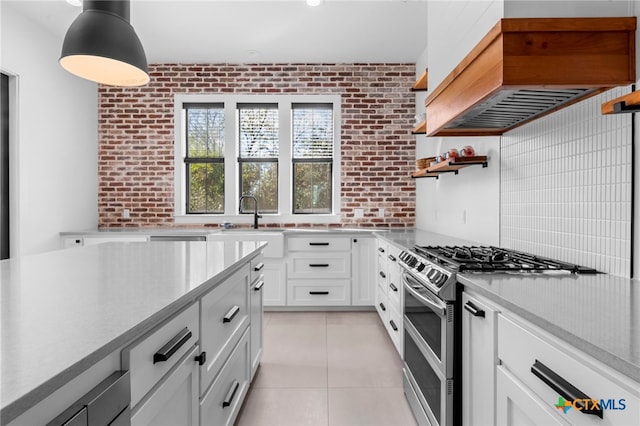 kitchen with high end range, custom range hood, white cabinetry, and brick wall