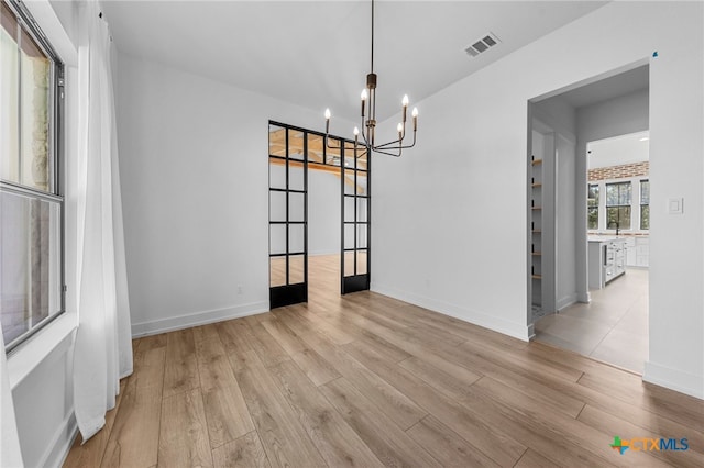 unfurnished dining area with french doors, light wood-type flooring, and a notable chandelier