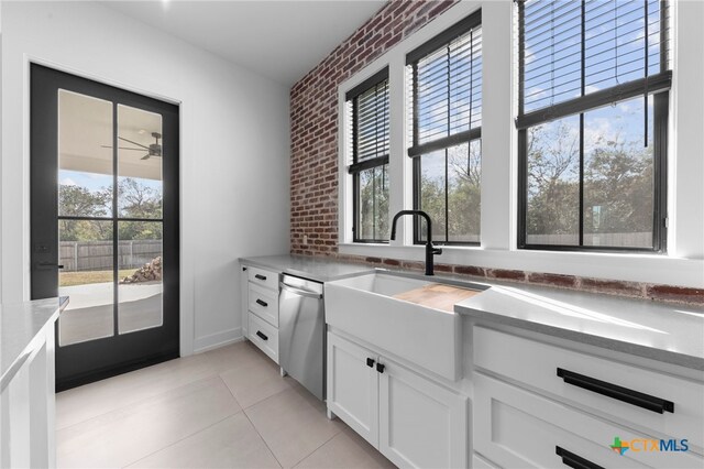 kitchen with dishwasher, sink, light tile patterned flooring, brick wall, and white cabinets