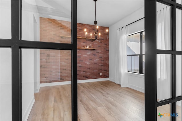 unfurnished dining area with light hardwood / wood-style flooring, a notable chandelier, and brick wall