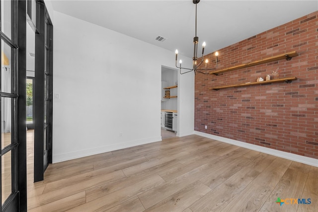 unfurnished dining area featuring light hardwood / wood-style floors, beverage cooler, brick wall, and an inviting chandelier