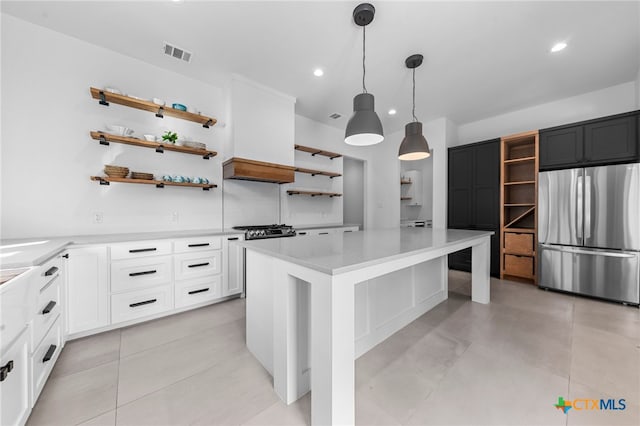 kitchen featuring stainless steel refrigerator, a center island, light tile patterned floors, decorative light fixtures, and white cabinets