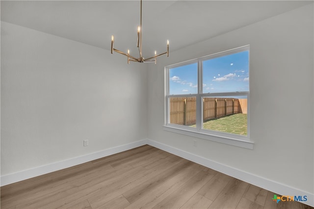 empty room with light hardwood / wood-style flooring and an inviting chandelier