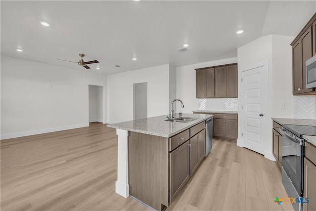 kitchen featuring decorative backsplash, an island with sink, light hardwood / wood-style floors, light stone counters, and stainless steel appliances