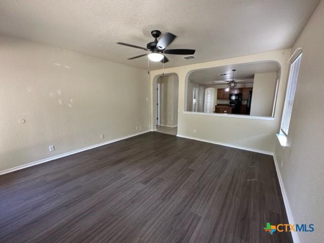 221 Roadrunner Ave, New Braunfels, TX 78130 - unfurnished living room featuring a ceiling fan, arched walkways, dark wood finished floors, and a textured ceiling