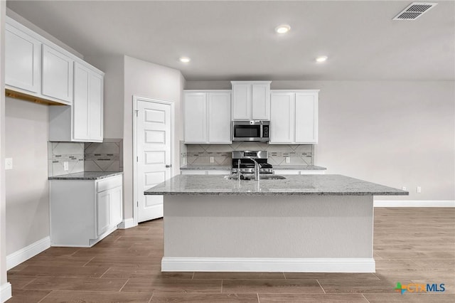 kitchen with stainless steel appliances, light stone counters, dark hardwood / wood-style floors, a center island with sink, and white cabinets