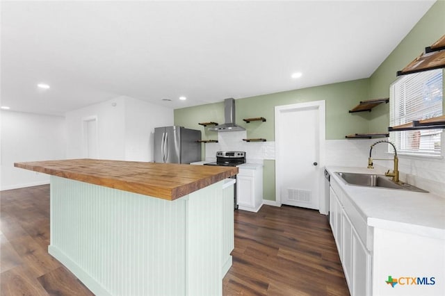 kitchen with butcher block counters, sink, a center island, appliances with stainless steel finishes, and wall chimney range hood