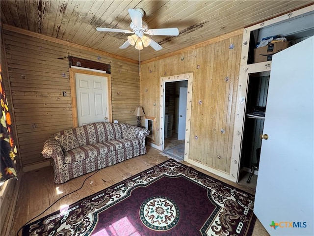 living area featuring wood ceiling, wood finished floors, a ceiling fan, and wood walls