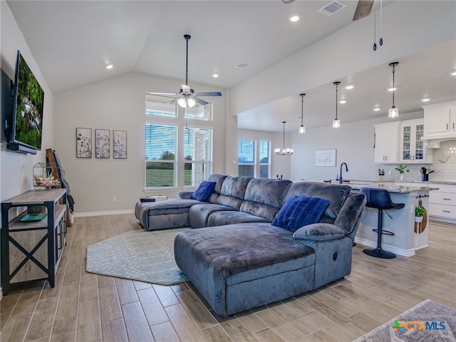 living room featuring ceiling fan with notable chandelier, light hardwood / wood-style floors, lofted ceiling, and sink