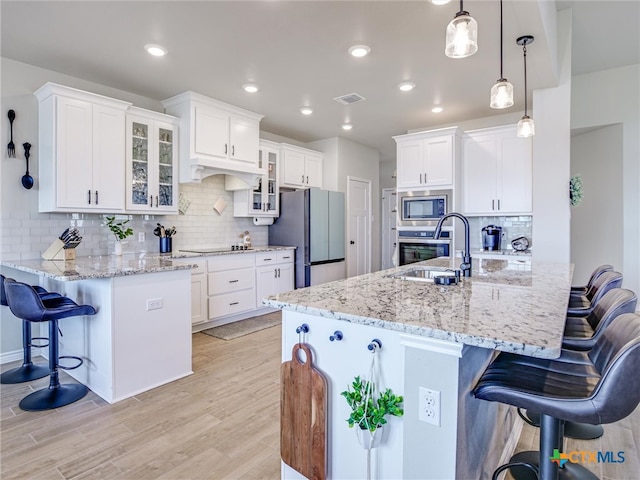 kitchen featuring stainless steel appliances, white cabinets, a kitchen breakfast bar, pendant lighting, and light hardwood / wood-style flooring