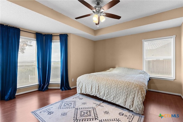 bedroom with dark hardwood / wood-style floors, a raised ceiling, and ceiling fan