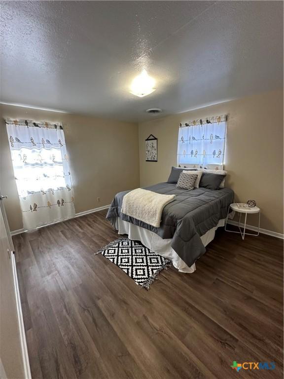 bedroom with baseboards, a textured ceiling, visible vents, and wood finished floors