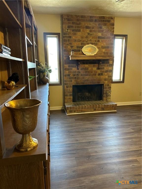 living area featuring dark wood-style floors, a brick fireplace, a textured ceiling, and baseboards