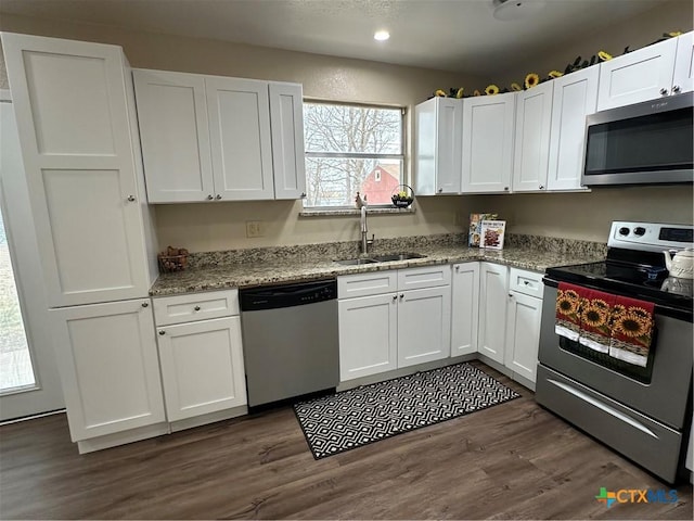 kitchen with white cabinets, dark wood-style floors, light stone counters, appliances with stainless steel finishes, and a sink