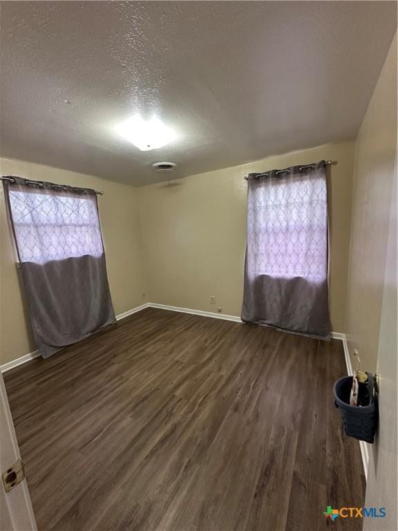 unfurnished room featuring a textured ceiling, dark wood-style flooring, and baseboards