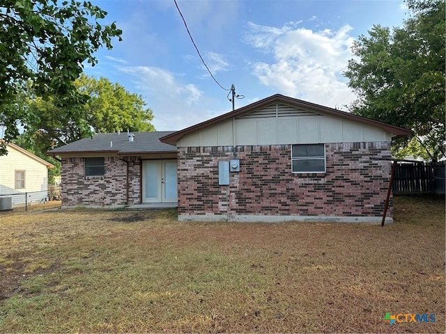 back of house featuring brick siding, a lawn, and fence