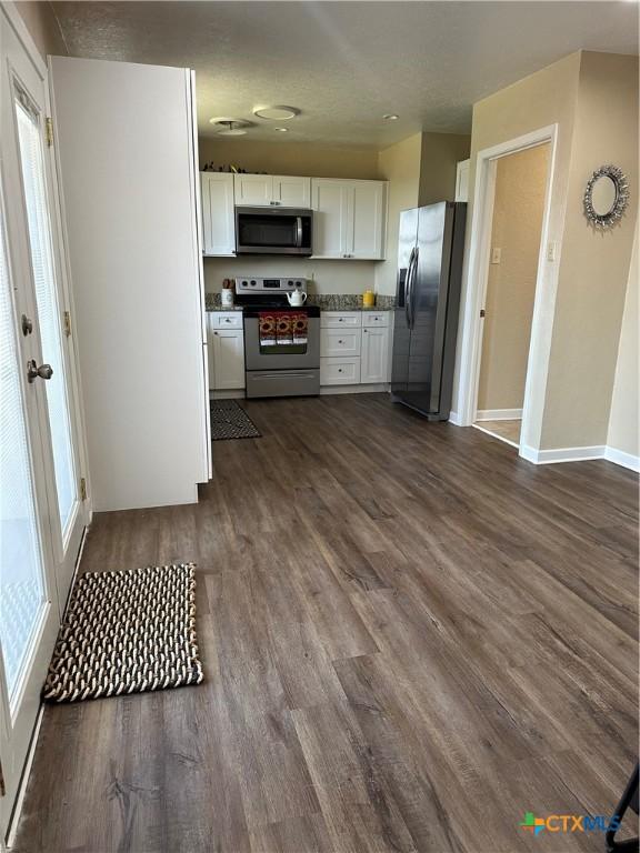 kitchen featuring stainless steel appliances, dark wood-style flooring, white cabinetry, baseboards, and dark countertops