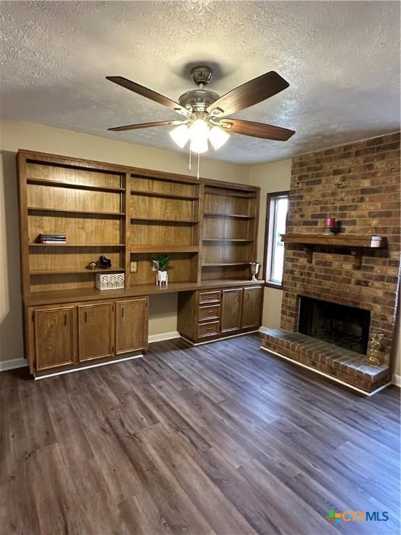 unfurnished living room featuring dark wood-type flooring, ceiling fan, a brick fireplace, and a textured ceiling