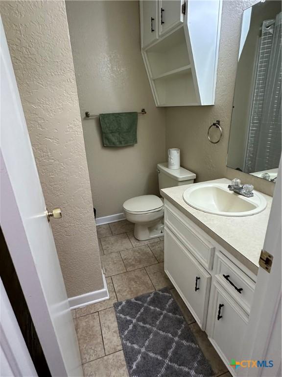 bathroom featuring baseboards, a textured wall, toilet, tile patterned floors, and vanity