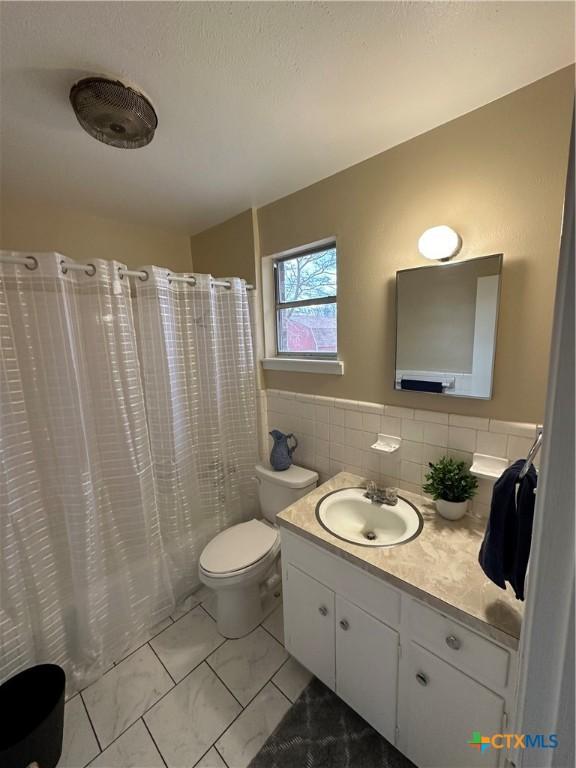 bathroom with curtained shower, marble finish floor, vanity, and tile walls