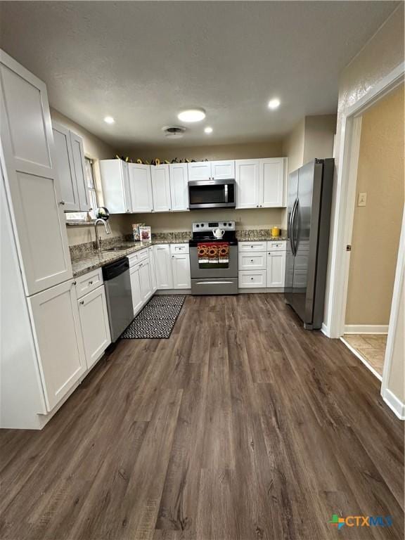 kitchen featuring dark wood finished floors, appliances with stainless steel finishes, light stone countertops, white cabinetry, and a sink