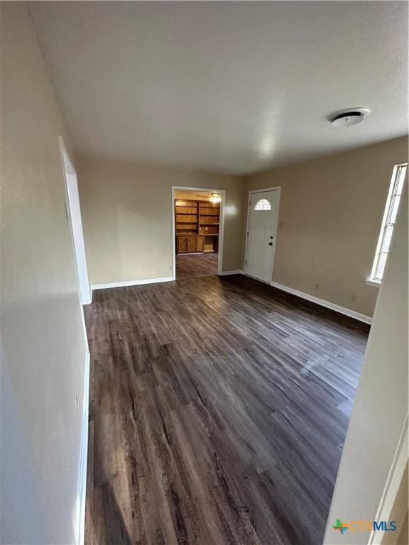 unfurnished living room with baseboards and dark wood-style flooring