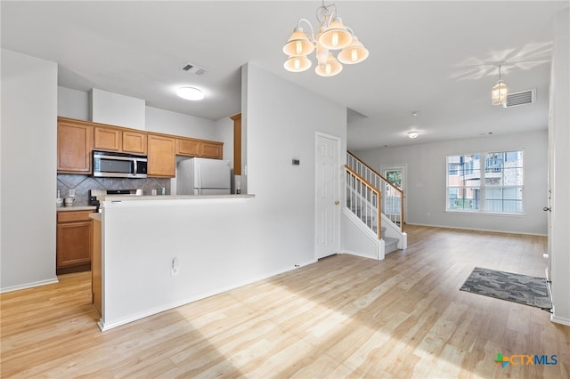 kitchen with light hardwood / wood-style floors, an inviting chandelier, hanging light fixtures, backsplash, and appliances with stainless steel finishes