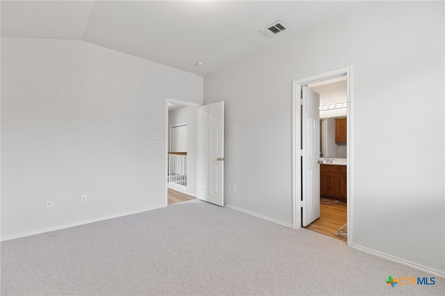 unfurnished bedroom with vaulted ceiling, light colored carpet, and ensuite bath