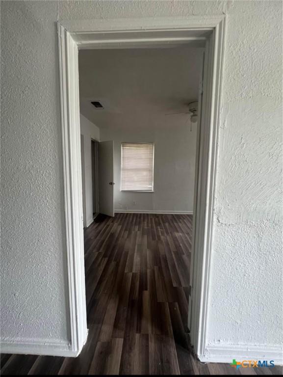 hallway featuring baseboards, a textured wall, and wood finished floors