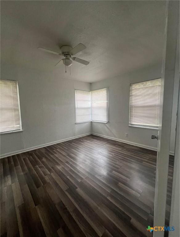 empty room with baseboards, ceiling fan, and dark wood-style flooring