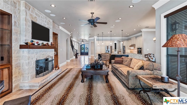 living room featuring a stone fireplace, ceiling fan, and crown molding