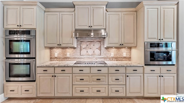 kitchen featuring stainless steel appliances, cream cabinetry, backsplash, and light stone countertops