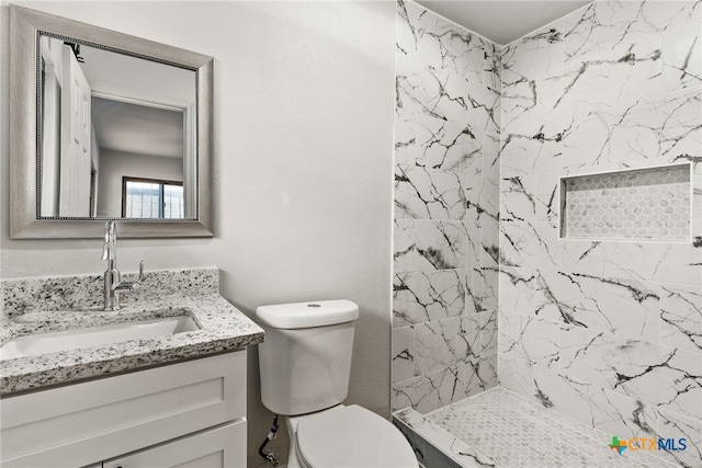 bathroom featuring a tile shower, vanity, and toilet