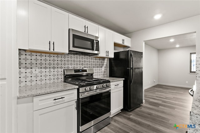 kitchen with hardwood / wood-style floors, backsplash, light stone countertops, white cabinetry, and stainless steel appliances